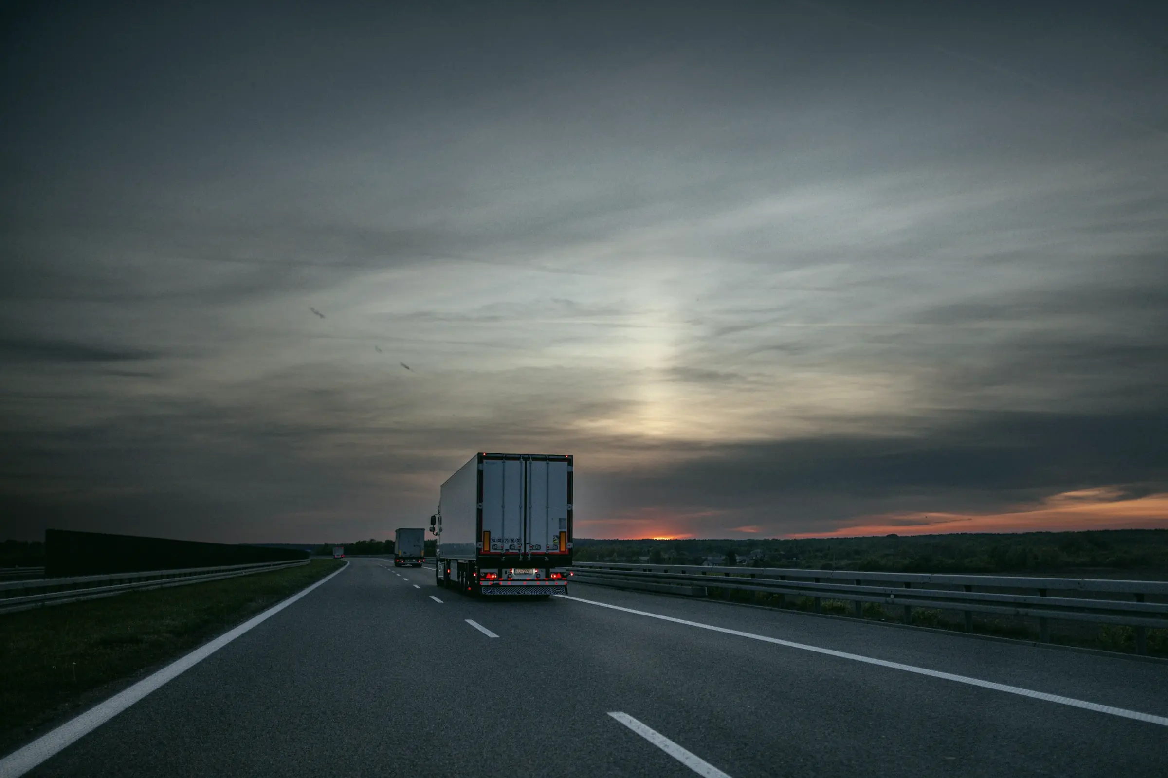 A lone tractor-trailer on an open highway at dusk